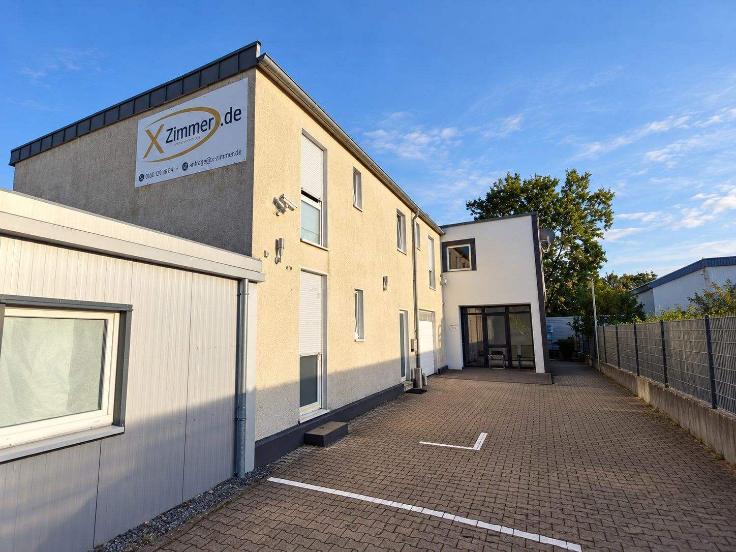 Das Haus in der Kieler Straße mit X-Zimmer-Schild, davor Hof mit markierten Stellplätzen.