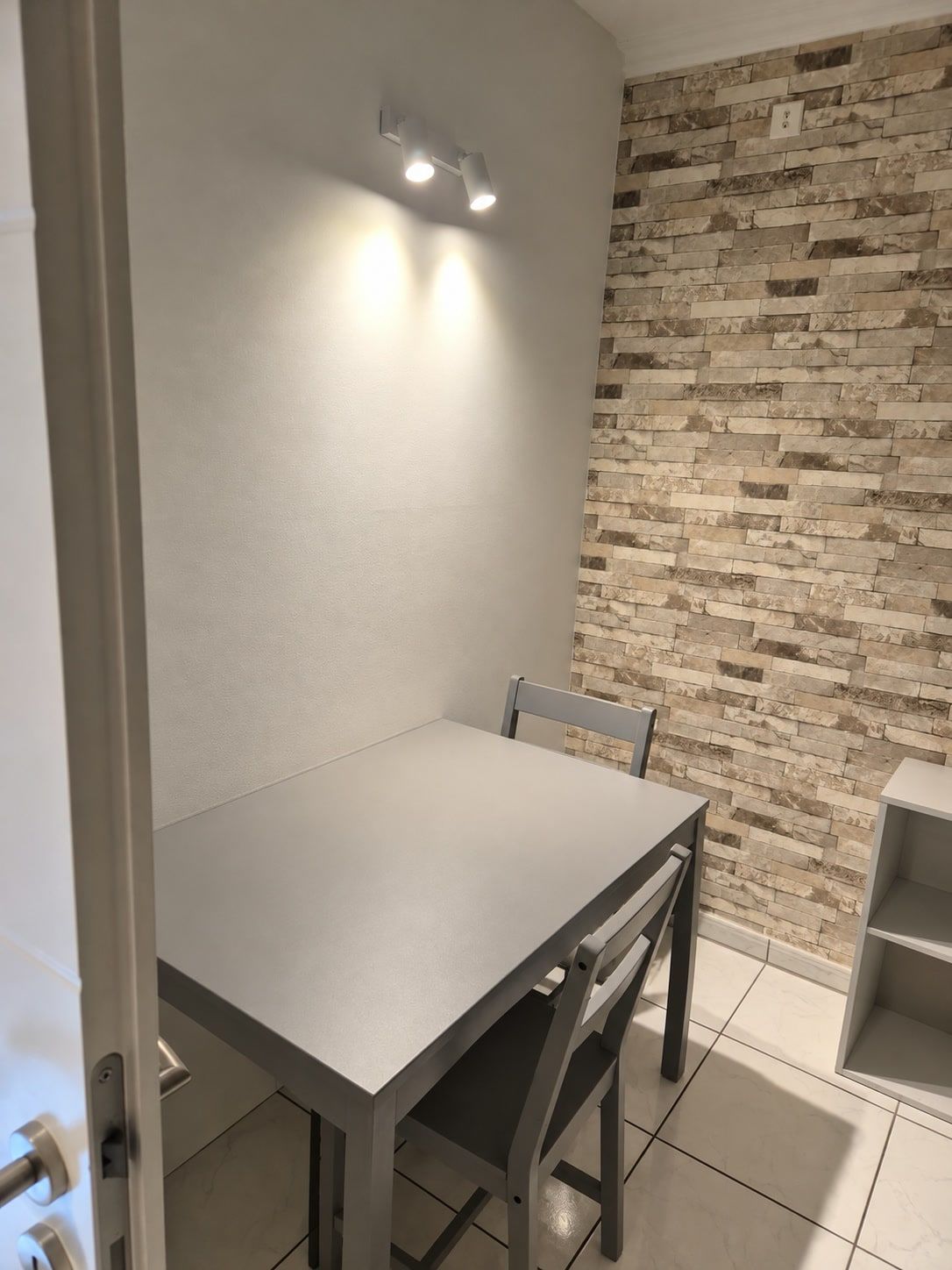 Grauer Esstisch mit zwei Stühlen neben der Tür, dahinter die Wand in Steinoptik.