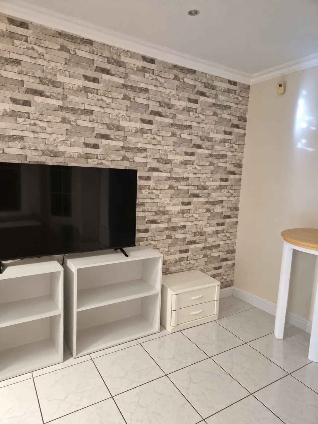 Großer Fernseher auf weißen Regalen vor einer Wand in Steinoptik.