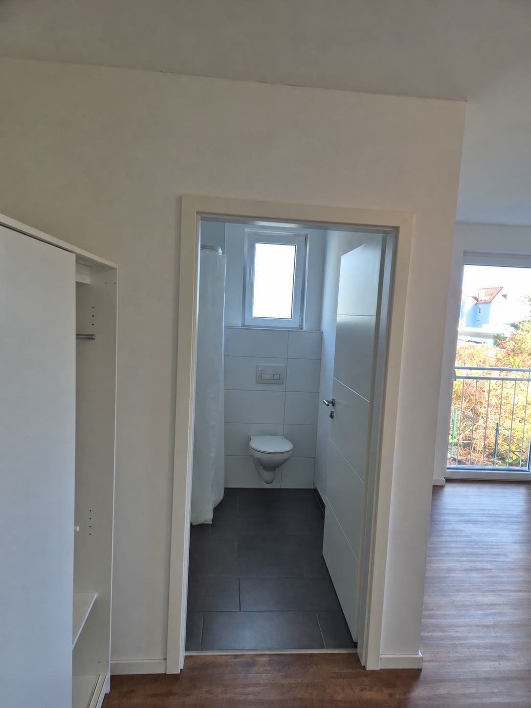 Blick durch die offene Tür ins eigene Bad mit WC und kleinem Fenster, links der offene Schrank.